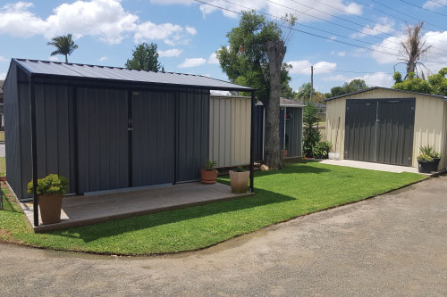 Couple of Gardens sheds built with different features and colours. One is an all grey shed with a roof. The other is a cream shed with dark grey doors by New Look Shed City